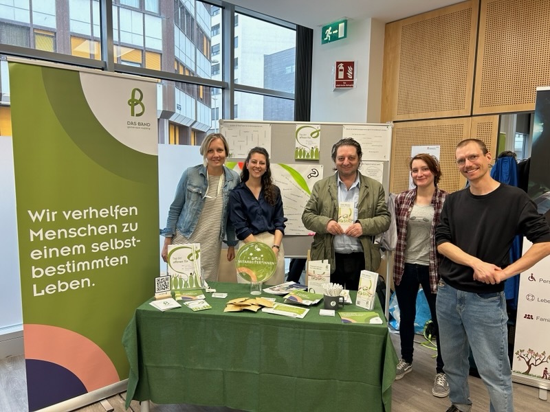 Team und ein Nutzer von DAS BAND mit ihrem Stand und Marketingmaterialien, 5 Personen
